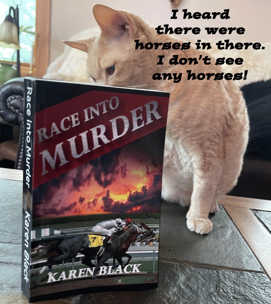 A cat curiously inspects a book titled 'Race Into Murder' by Karen Black, which features a horse racing scene on the cover.